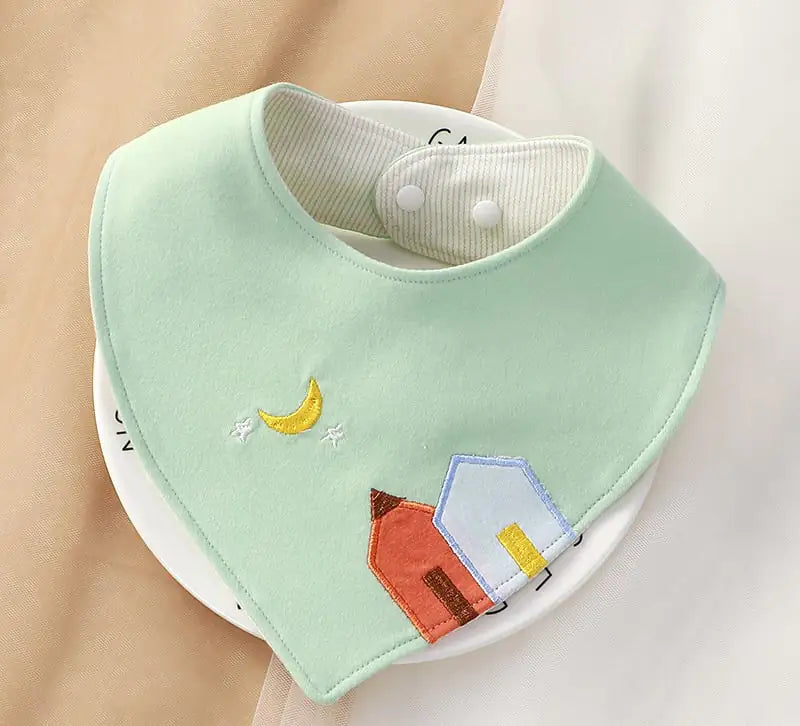 Light green baby bib with embroidered houses and a moon on a white background